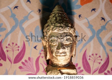 A golden Buddha head on a colored paper background.