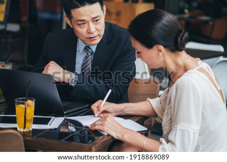 Business people working together. Serious businessman with laptop talking to businesswoman with papers and pen. Business partners having successful meeting in modern cafe