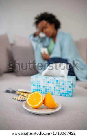 Sick woman lying in bed with high fever and a flu. Lemon and pills set around the tsofa, focus on the lemon. Sick Woman. Flu. Woman Caught Cold. Headache. Virus 