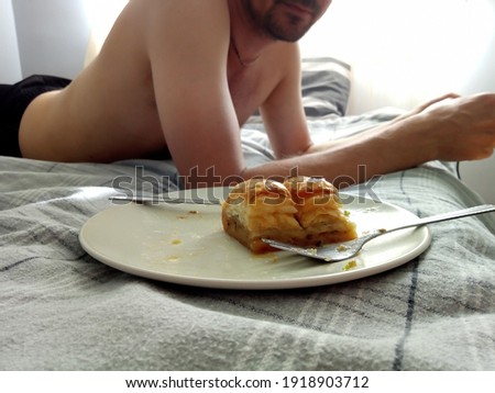 Romantic breakfast for a couple. Sweet Turkish delight baklava on a plate over dark grey linen on the bed. Sunny morning, a young man lying in the background