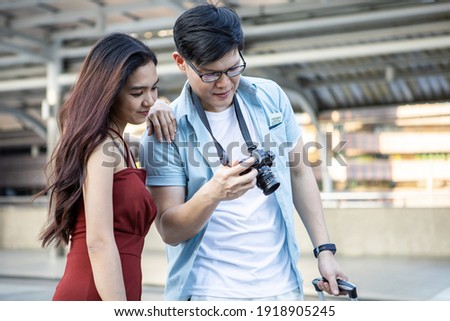 Asian young couple making a reservation look at the camera screen to see the picture after taking the picture while touring the city with happy.