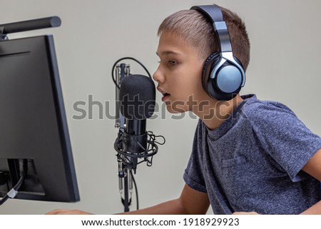 Boy talks looking to computer monitor screen. Kid wearing headphones using microphone. Online learning, remote education, gaming, podcast