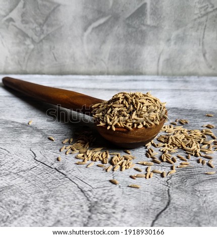 cumin seeds in wooden spoon with grey background