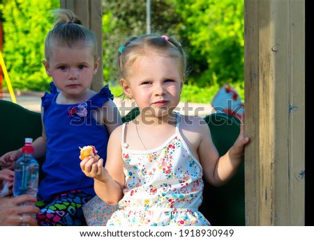 Little girls eat a bun on the playground. Lunch after active games