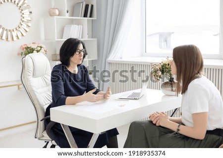 two young women conduct a coaching session in a home office in a light interior with a laptop and flowers on the table, the concept of remote work and psychological counseling Royalty-Free Stock Photo #1918935374