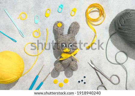 Easter crafting DIY. Handmade knitted toy Easter rabbit, and needlework accessories on grey background. Overhead view, flat lay
