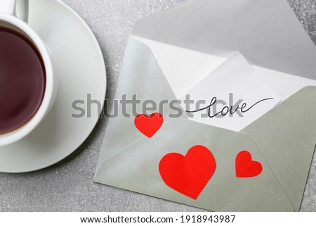 Card with handwritten word love in envelope near cup of coffee on grey table, flat lay