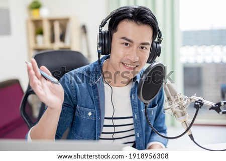 asian man with headphones and microphone recording podcast at studio with laptop