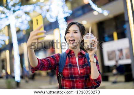 smiling asian female traveler holds a cup of bubble tea and take selfie on the street while vacation in Taiwan
