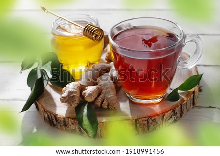 Still-life with honey and fresh tea with bee shadow in a transparent tea cup on white wooden background