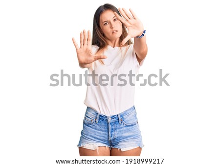 Beautiful caucasian woman wearing casual white tshirt doing frame using hands palms and fingers, camera perspective 