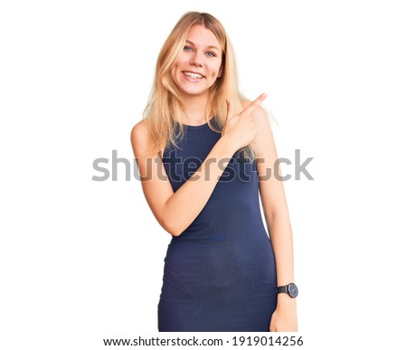 Young beautiful blonde woman wearing casual dress cheerful with a smile of face pointing with hand and finger up to the side with happy and natural expression on face 