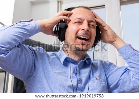 Man smiling at the camera as he sits recording a podcast on his laptop computer with headphones. Smiling man operator working in call center and support people. Manager communicating with client.