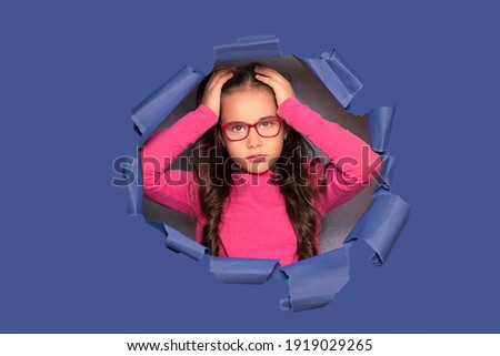 Little girl with glasses on a blue background in the studio