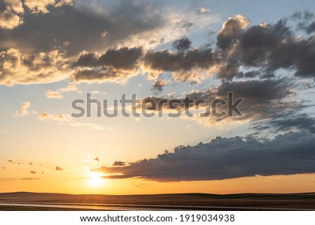 Sunset theme for sky replacement background with dark themed clouds, blue sky and sun shining on the horizon. Great for tranquil, calm, serene themed art.