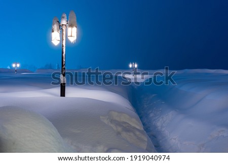 Night photography of a footpath in deep snow and lanterns in ice