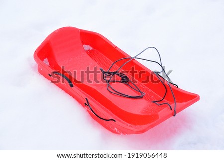 Red plastic sled on snow in a city park