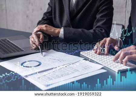 Two traders man and woman researching historic data to predict stock market behavior. Internet trading concept. Forex and financial hologram chart over the table with the documents Royalty-Free Stock Photo #1919059322