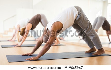 Portrait of focused man making yoga exercises with friends at fitness center Royalty-Free Stock Photo #1919065967