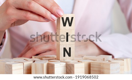 The word Win on a wooden toy blocks with womans hands, pink background. Business concept.