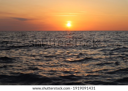 Bright orange sky, clouds and sun at sunset, the silhouette of the Stromboli volcano on the horizon, sun glare on the sea surface on an autumn evening, Calabria, Italy