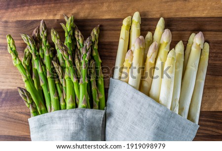 raw fresh bunch of green and white asparagus in grey cloth on rustic wood board Royalty-Free Stock Photo #1919098979
