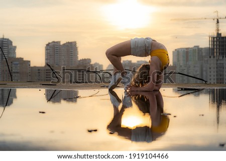Flexible female gymnast making trick with reflection in the water during dramatic sunset