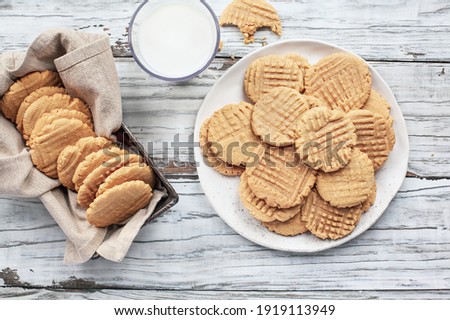 Flatlay of fresh baked, homemade peanut butter cookies and milk over a white rustic table. Image shot from up above, top view.