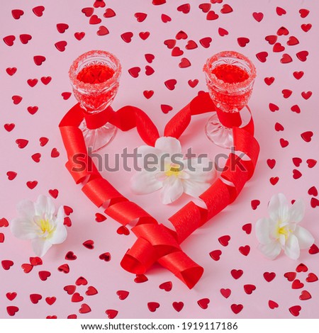 Background to the concept of International Women's Day. Creative arrangement made of 2 glasses with red drink, heart, white flowers. Bright pink background.