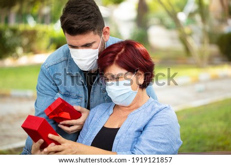 Mom and son hugging and gifts. Mature woman and her son in medicine masks protecting from viruses. Son is giving his mother a mother's day gift.