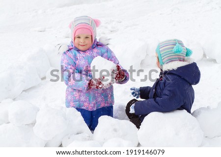 Two cute little girls in winter overalls are playing in the snow in winter, selective sharpness, special blur.
