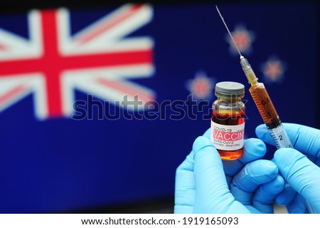 COVID-19 vaccine. Hands in blue medical gloves holding a vaccine bottle and syringe with New Zealand flag as background