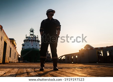 Marine Deck Officer or Chief mate on deck of offshore vessel or ship , wearing PPE personal protective equipment - helmet, coverall. Ship is on background Royalty-Free Stock Photo #1919197523