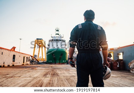 Marine Deck Officer or Chief mate on deck of offshore vessel or ship , wearing PPE personal protective equipment - helmet, coverall. Ship is on background Royalty-Free Stock Photo #1919197814