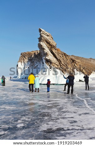 Frozen Lake Baikal. Beautiful icy Ogoy Island on sunny cold day. Groups of tourists and families with children come across the ice of Small Sea to take pictures on their mobile phones. Winter travel
