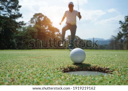 Blurred Golfer putting ball on the green golf, lens flare on sun set evening time. Golfer action to win after long putting golf ball in to the hole.                                Royalty-Free Stock Photo #1919219162