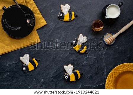 Bee sugar cookies with coffee, cream and honey against a black background.