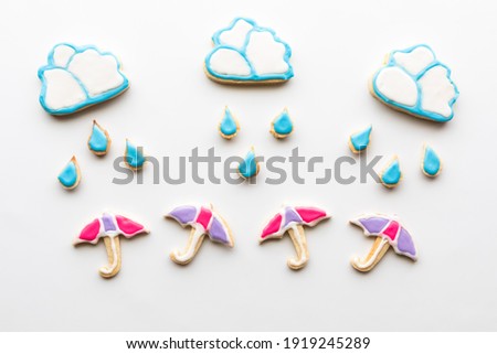 Sugar cookies in the shapes of clouds, raindrops and umbrellas against a white background. 