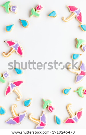 Umbrella, raindrops and tulip sugar cookies in a border frame with copy space in the middle.
