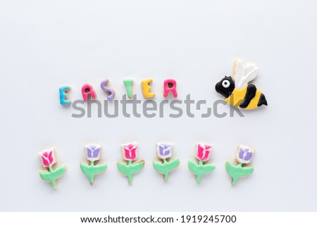 Sugar cookies in the shapes of tulips with a bee and the word Easter against a white background.