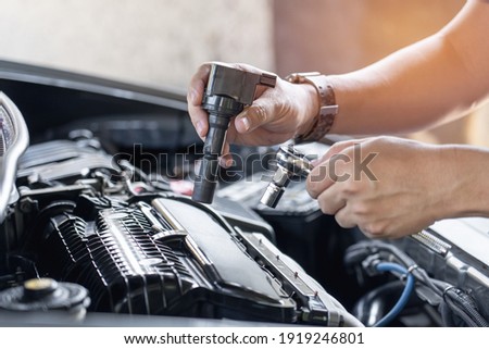 Close up spark plug coil in hand a man and use block wrench remove a bolt in service in garage and engine room  background