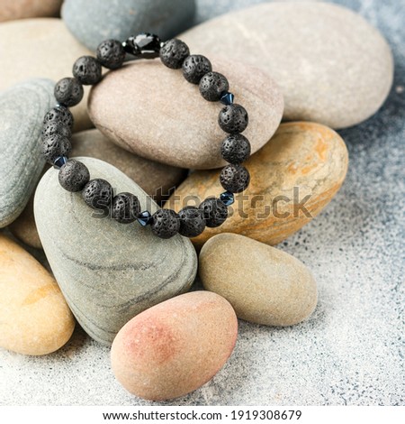 Beautiful bracelet made of natural black volcanic lava. Jewelry made of round-shaped beads is placed on large sea stones. Selective focus, square picture