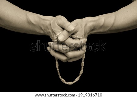 The man's sinewy hands are clasped together, fingering a rosary against a black, isolated background. Close-up, banner, copy space.