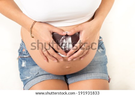 Close up of pregnant woman holding ultrasound scan on her tummy