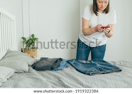 Woman taking photo of jeans on smartphone. Concept of secondhand, online sale, sustainability, sale of used