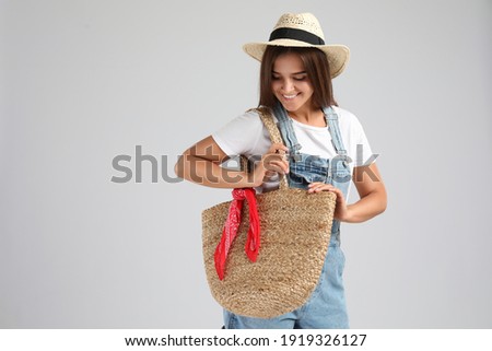 Young woman with stylish straw bag on light grey background