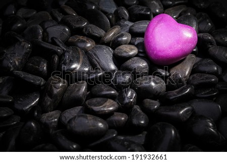 An illuminated pink heart lying on black stones