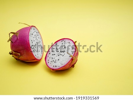 Two halves of dragon fruit with white flesh on a yellow background. Pink-skinned pitaya fruit is low in calories, packed with essential vitamins and minerals, contains dietary fiber. Copy space