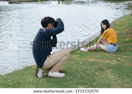 Male photographer take a photo of teenage model while sitting next to the lake in the park.