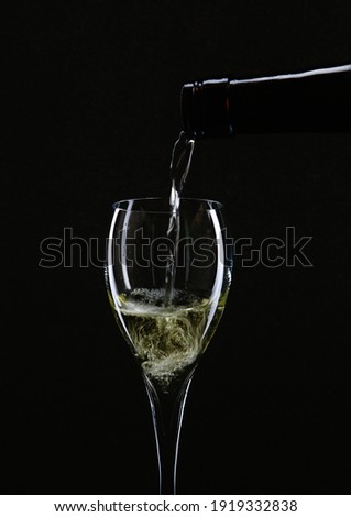 White wine pouring into a glass from a bottle on a black background, selective focus. High quality photo
